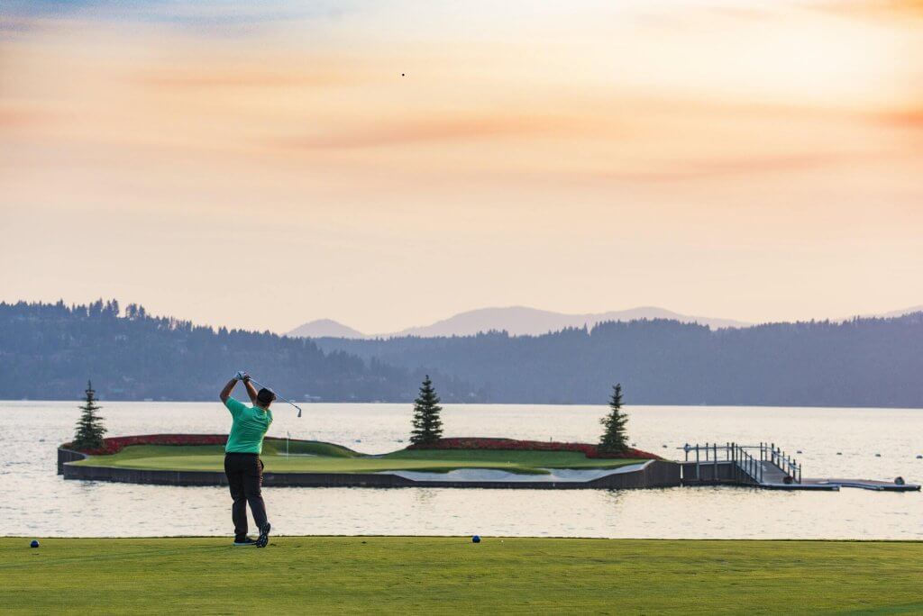 A man swings a golf club on a course near a lake.