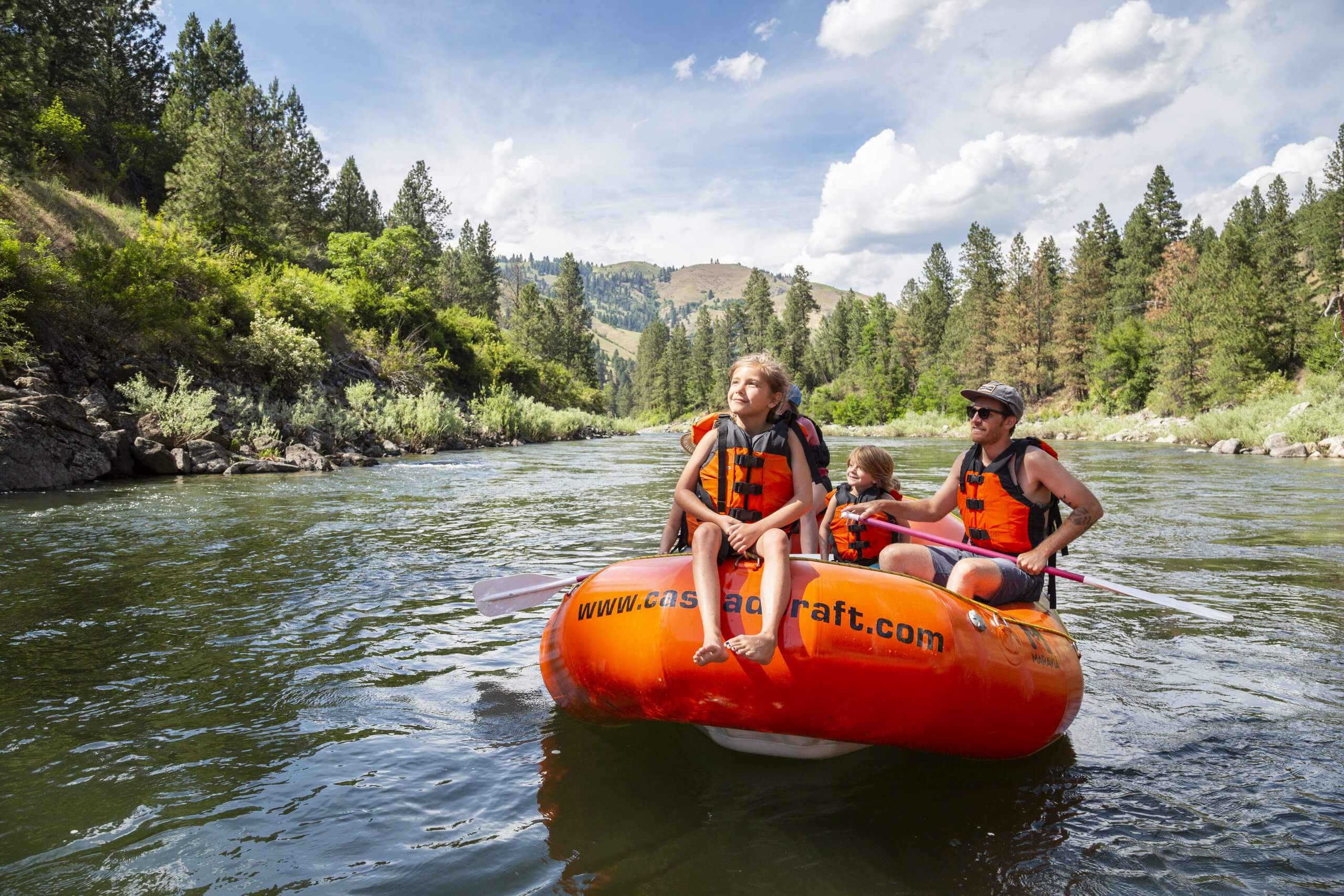 a family rafting on a river lined with trees