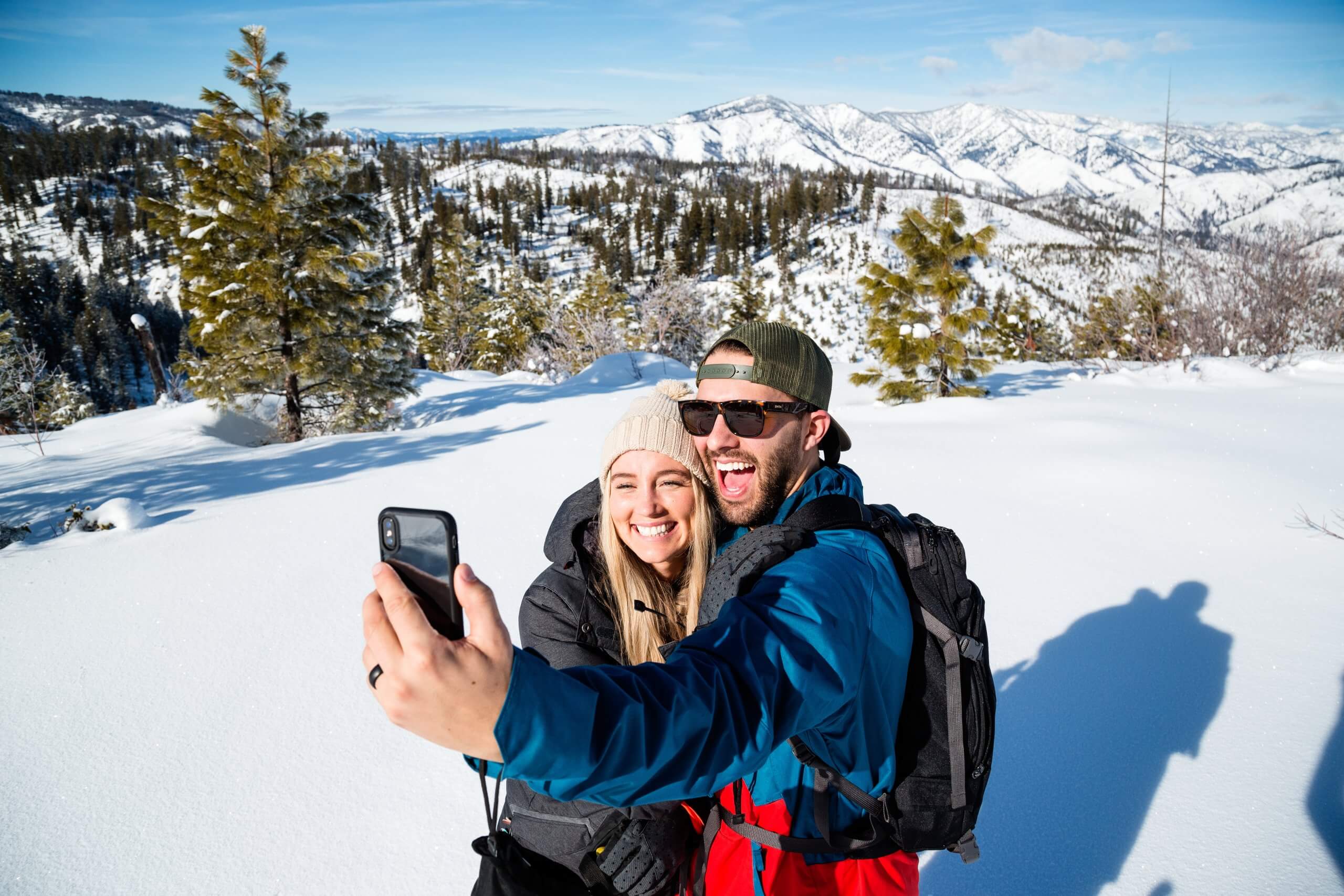 A couple taking a selfie while hiking along the Whoop Um Up Trail in the winter with mountains in the background.
