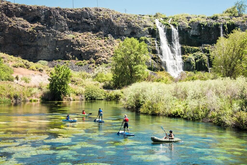 People paddleboarding and kayak near a waterfall at Ritter Island in Thousand Springs State Park.