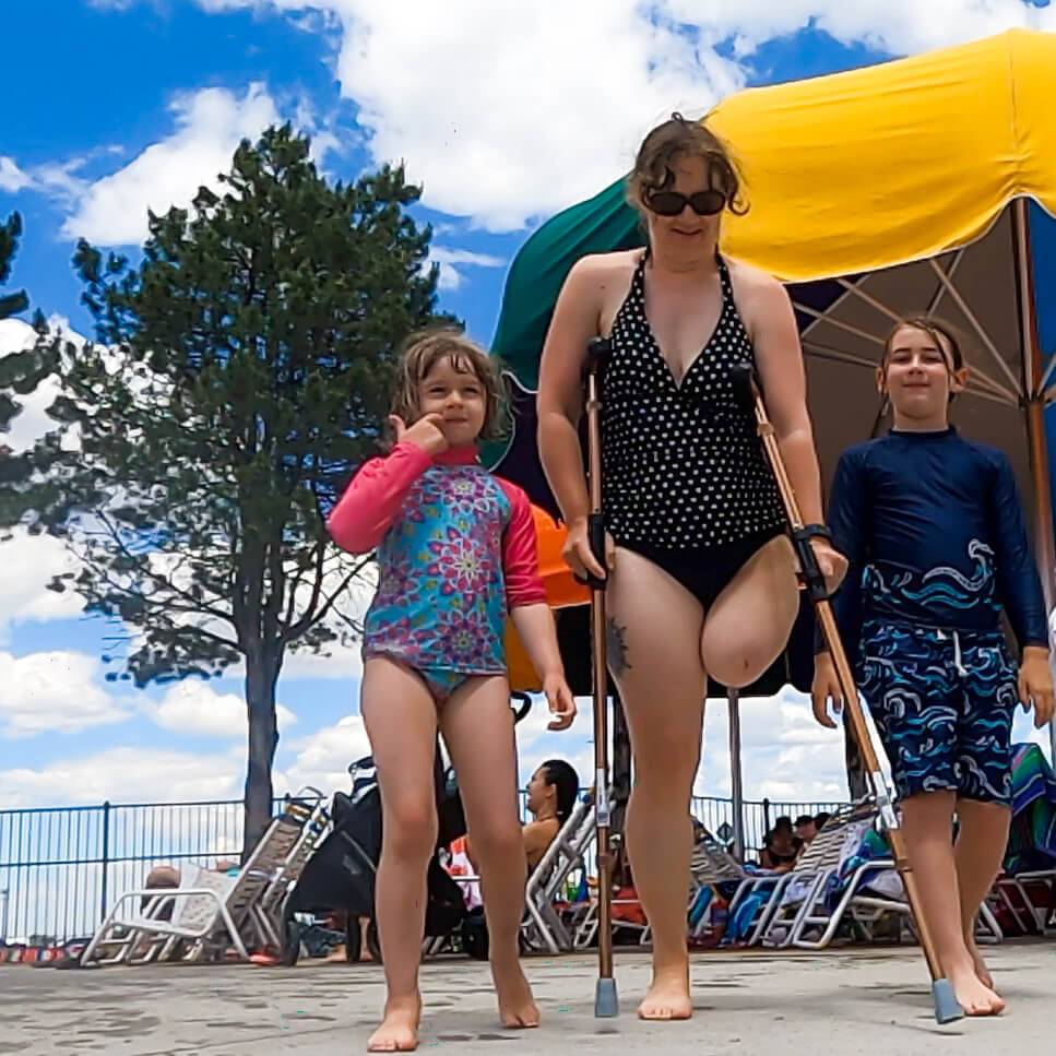 woman with one leg on crutches, with one of her children on each side, with everyone in swimsuits