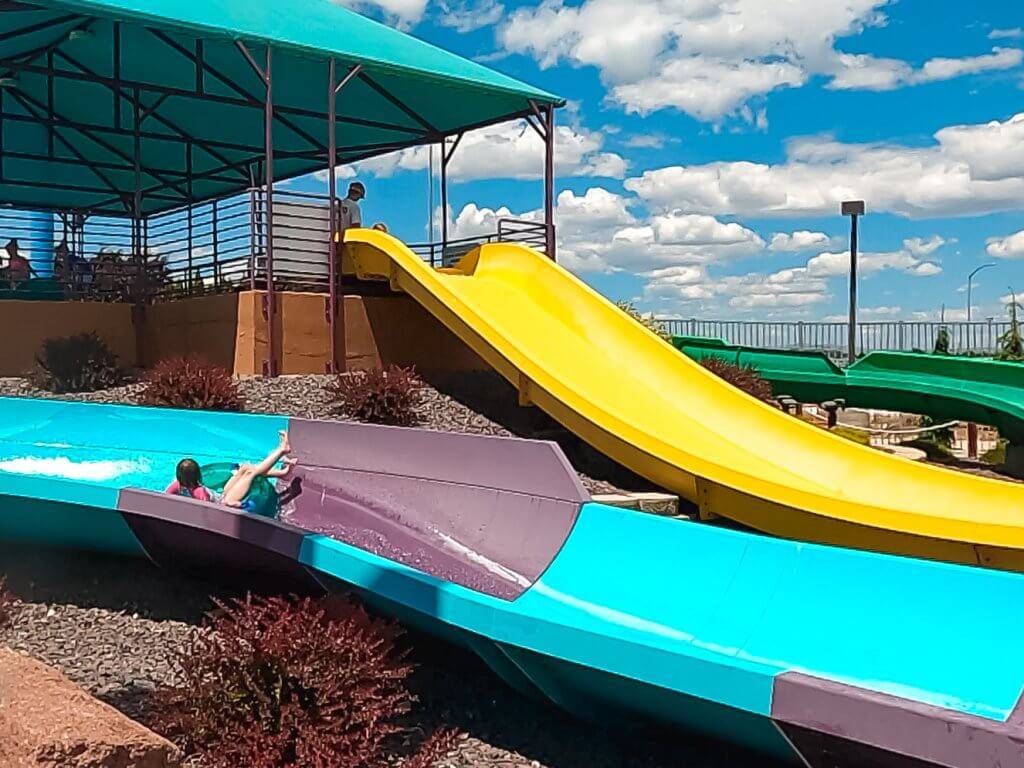 child on inflatable innertube coming down turquoise and purple water slide