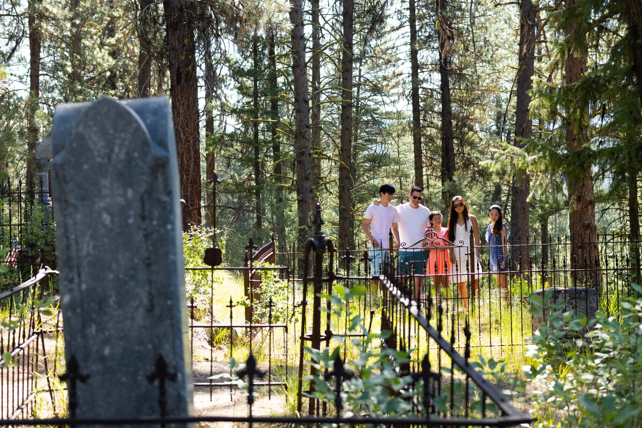 a family of five standing in the Idaho City Pioneer Cemetery, surrounded by tall trees