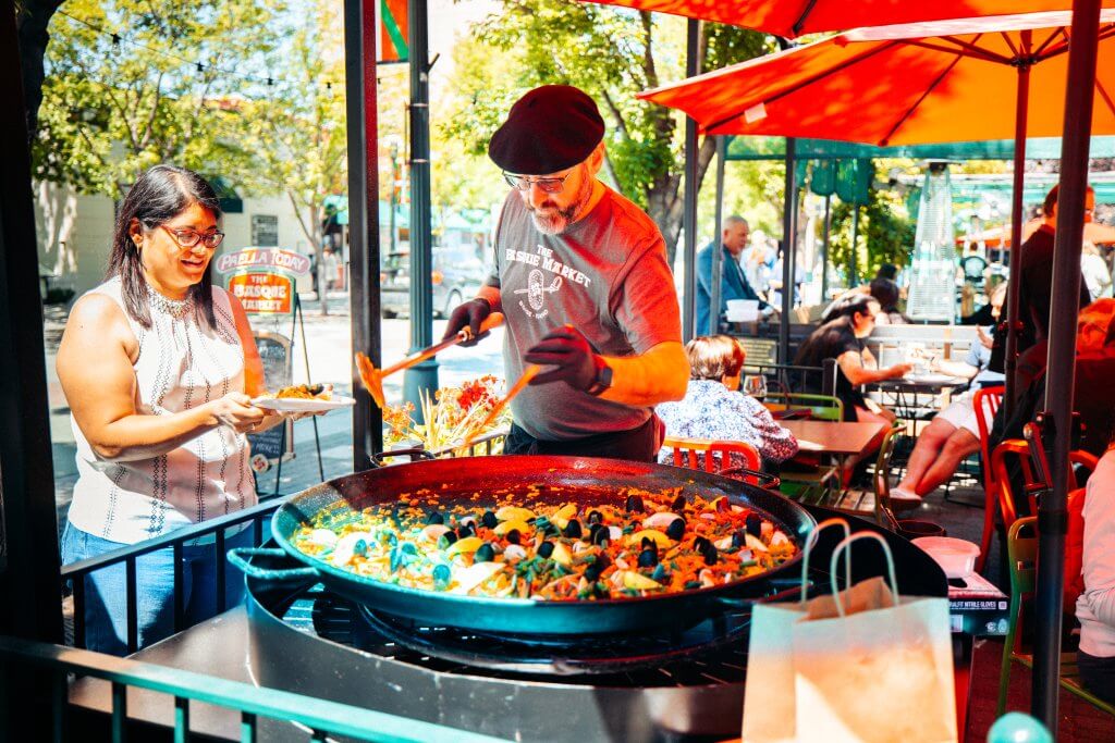 A man serving paella from a large pan to a woman at The Basque Market.