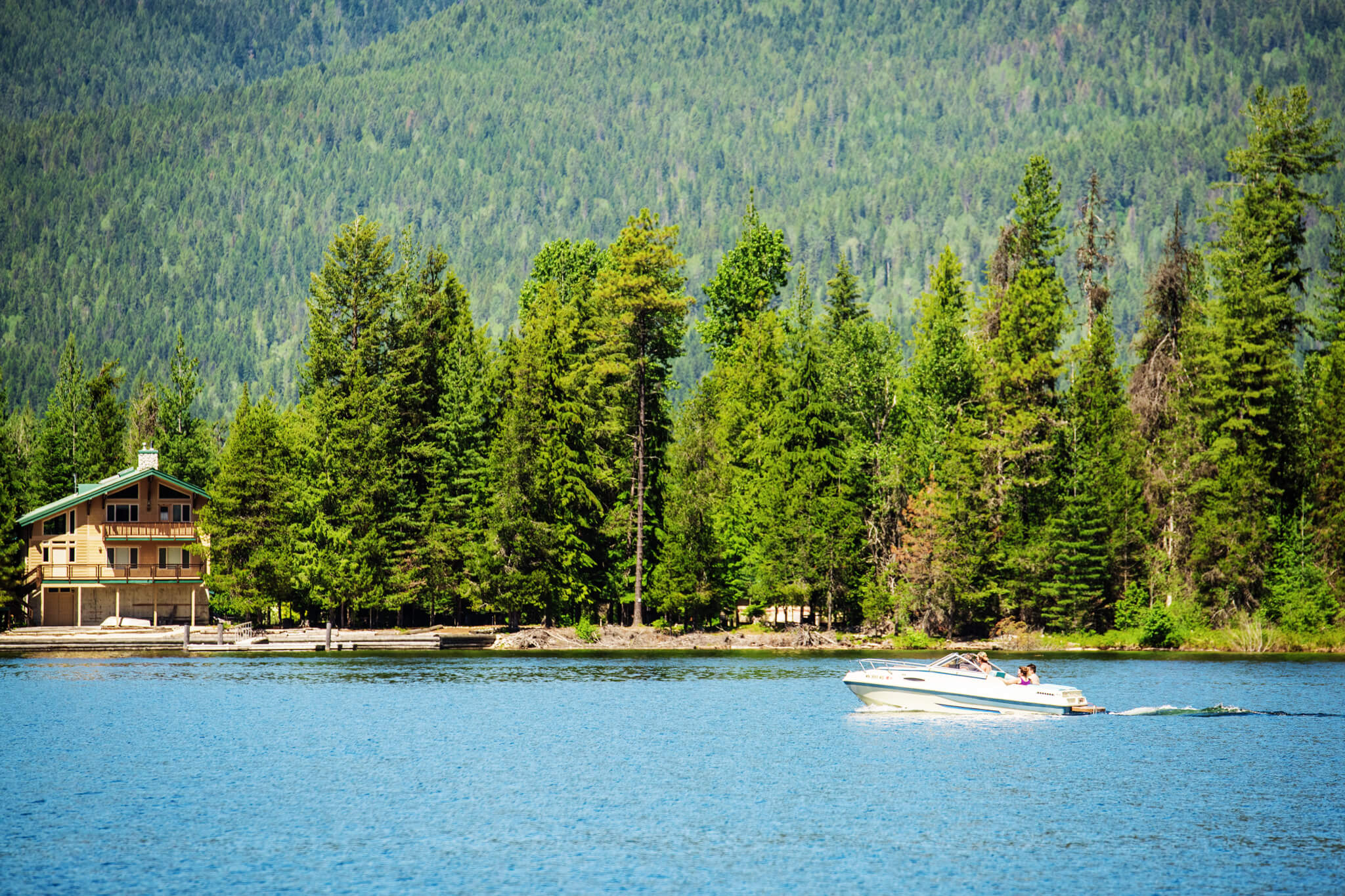 A group of people riding a jet boat across Priest Lake at Priest Lake State Park, and a forest of tall trees in the background..