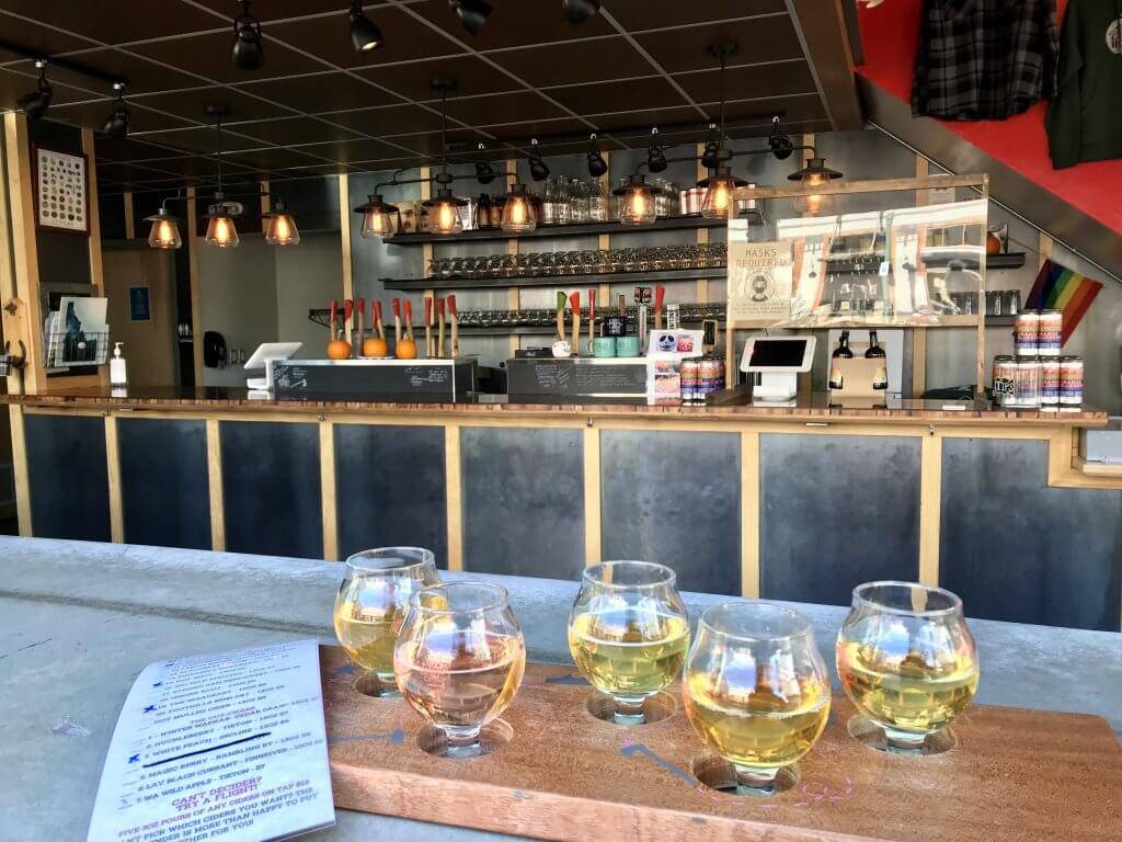 A menu and a flight of five ciders on a table with a bar in the background.