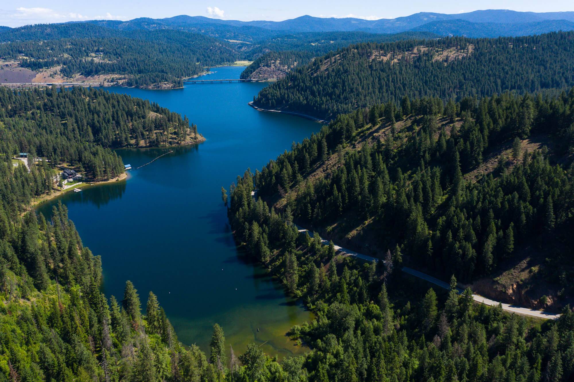 Aerial view of Lake Coeur d’Alene Scenic Byway with a map of Idaho that features an outline of the northern region overlaid. 