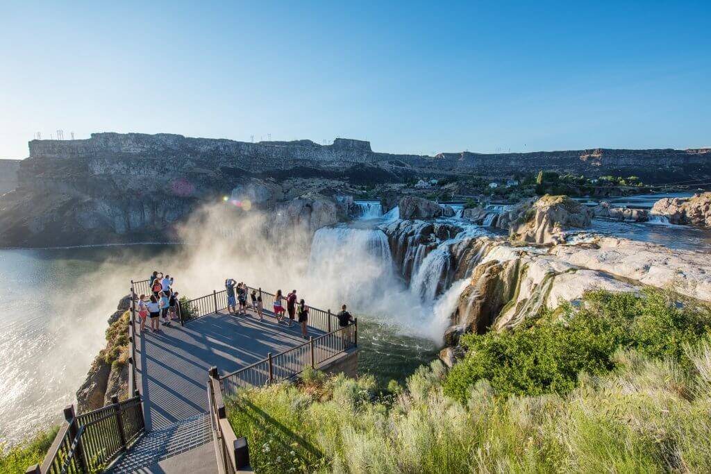 Shoshone Falls from the viewing deck in the summer with a map of Idaho that features an outline of the south central region overlaid. 