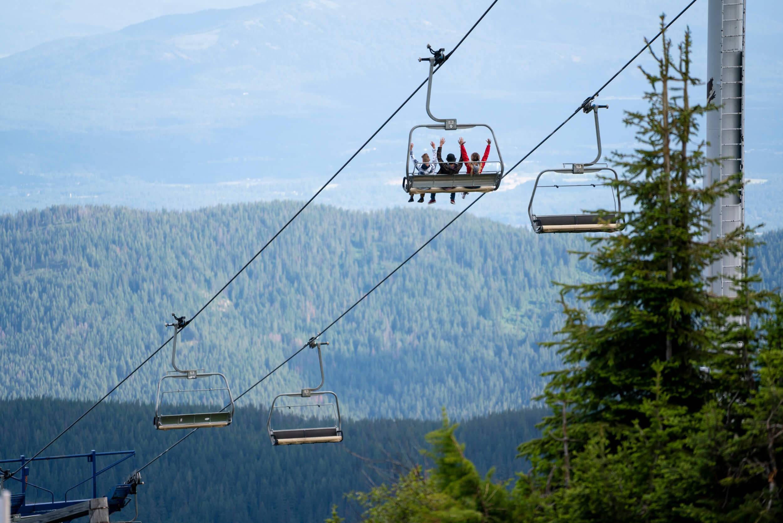 Three people ride a chairlift at a ski resort during the summer.