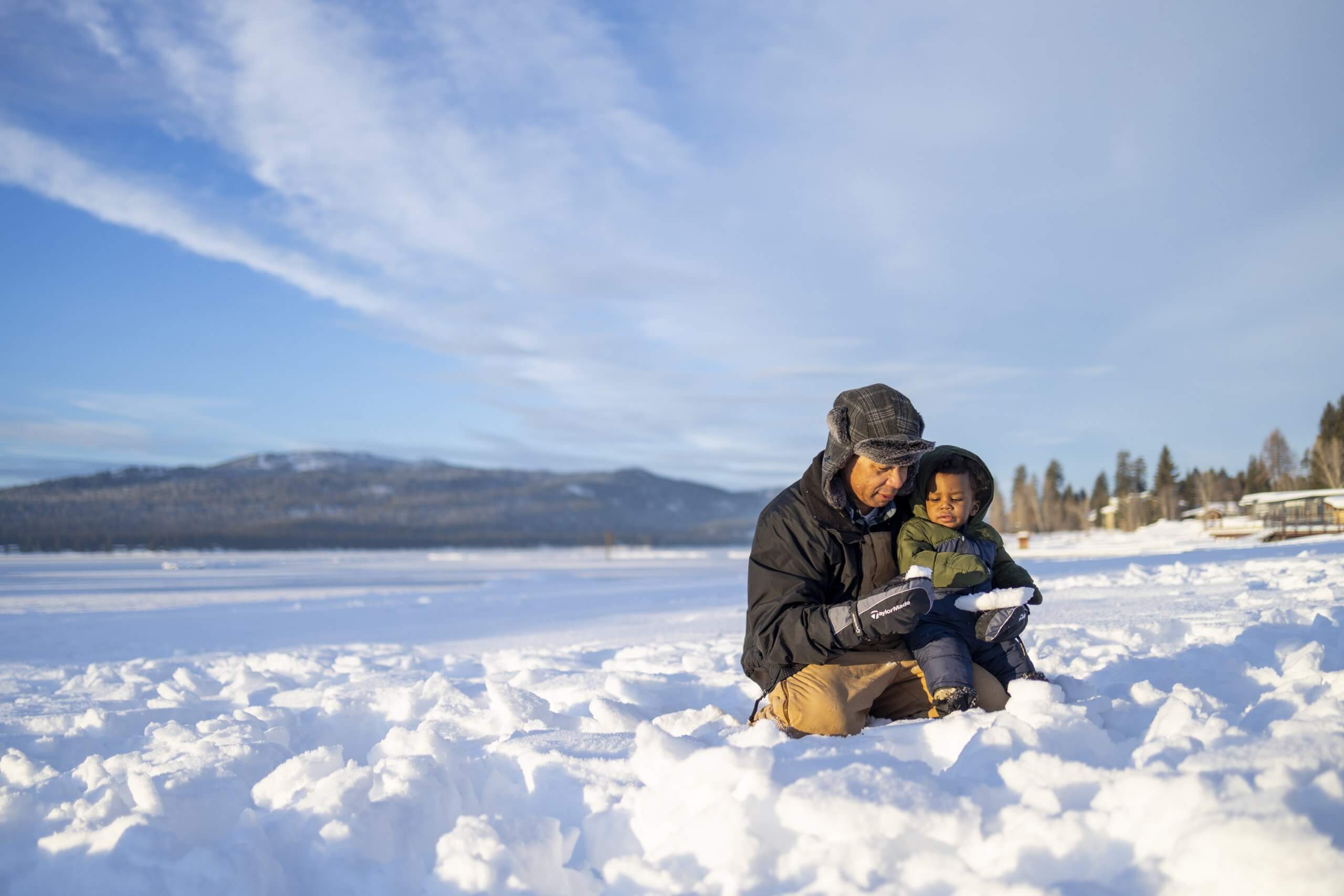 A parent and child in snow gear play in the snow on Payette Lake in the winter.