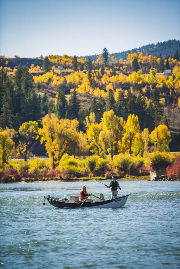 Two men cast lines from a drift boat in the South Fork of the Snake River, surrounded by fall colors.