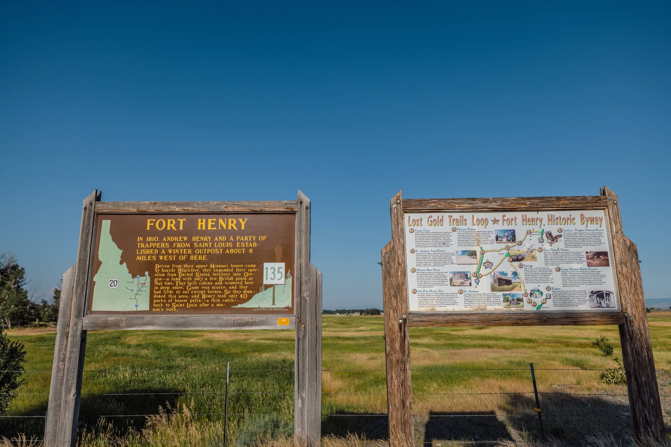 two wooden signs reading "fort henry" and "lost gold trails loop/fort henry historic byway" in from of a wide open field