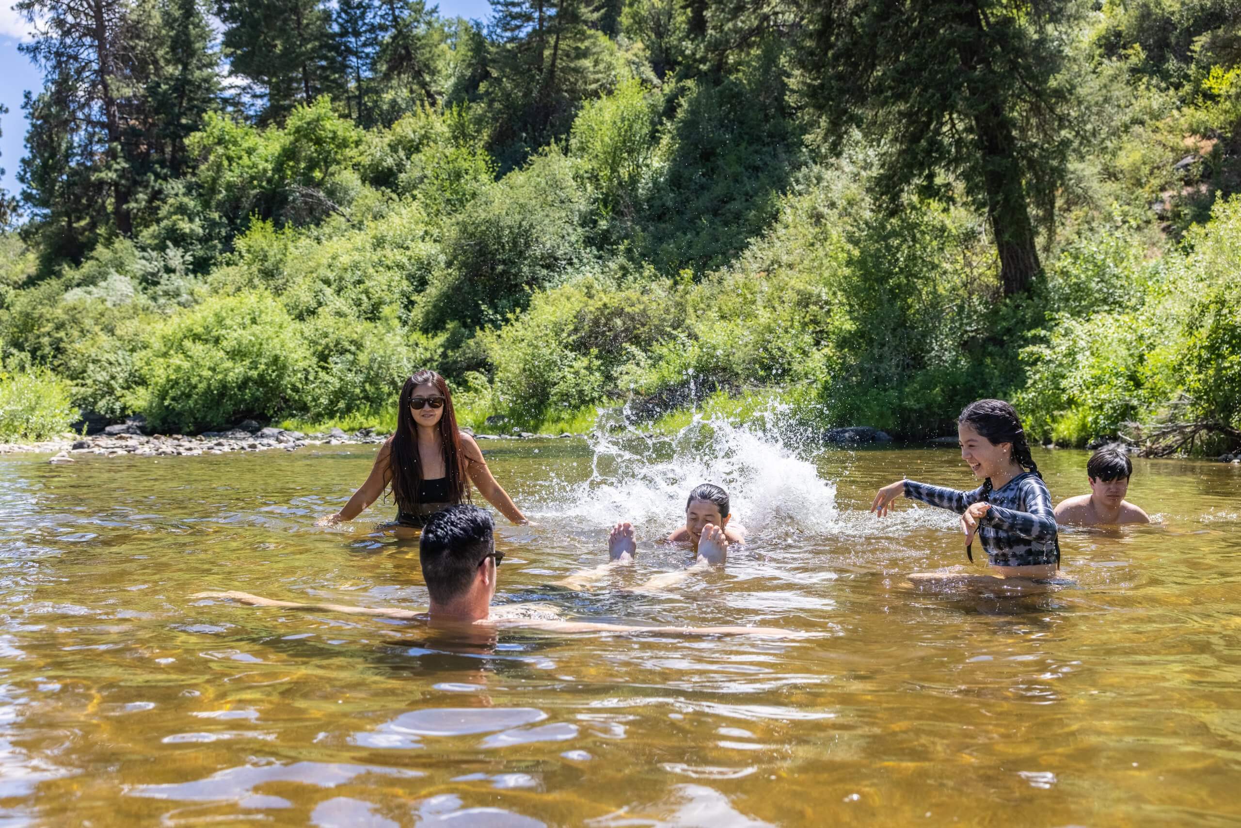 a group of people splashing in a creek surrounded by trees