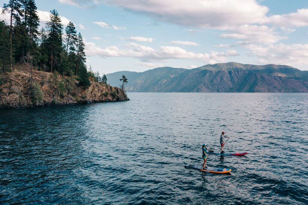 a man and woman on paddleboards with clear water on lake pend oreille