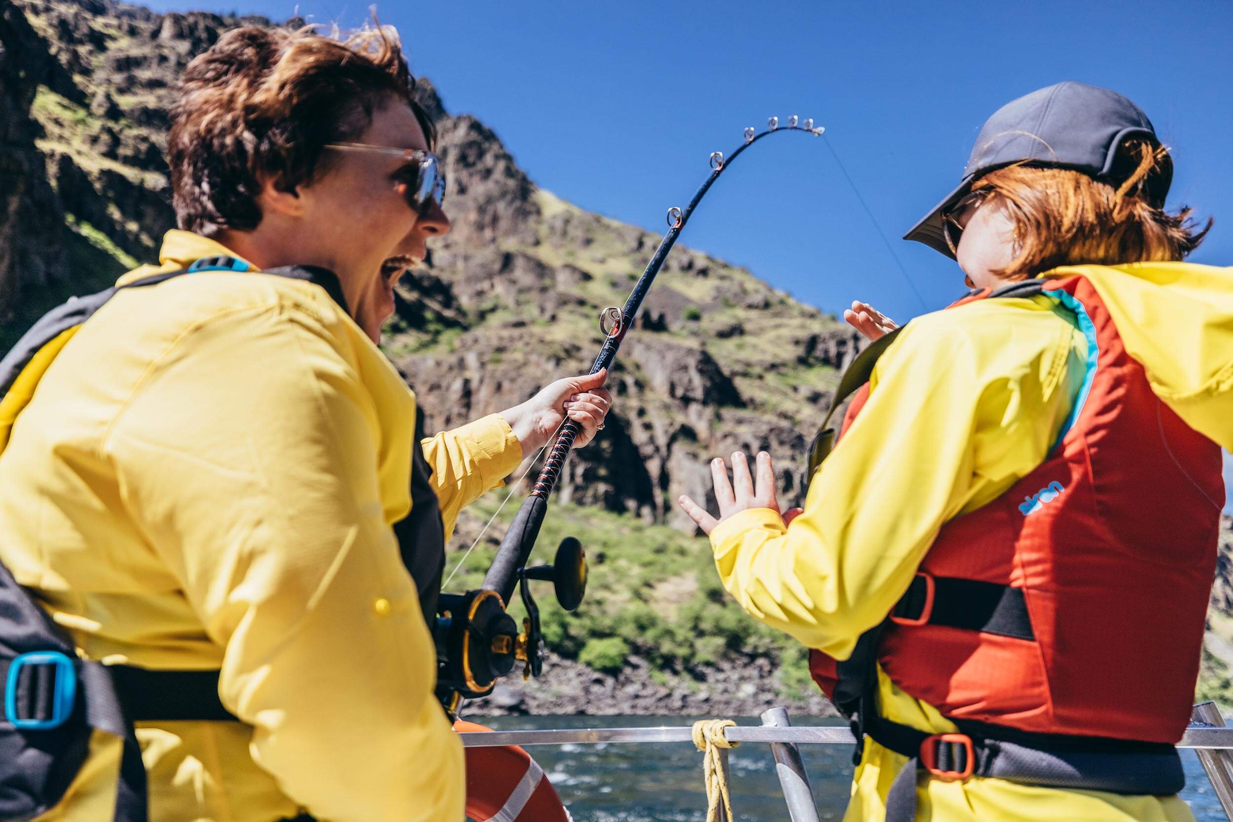 two people on a boat with a fishing rod on a river within a canyon