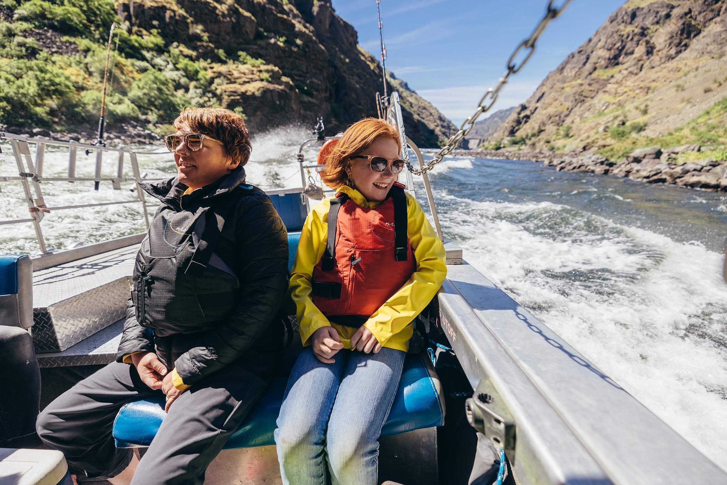 two people wearing life jackets sitting in a jet boat on a river within a canyon