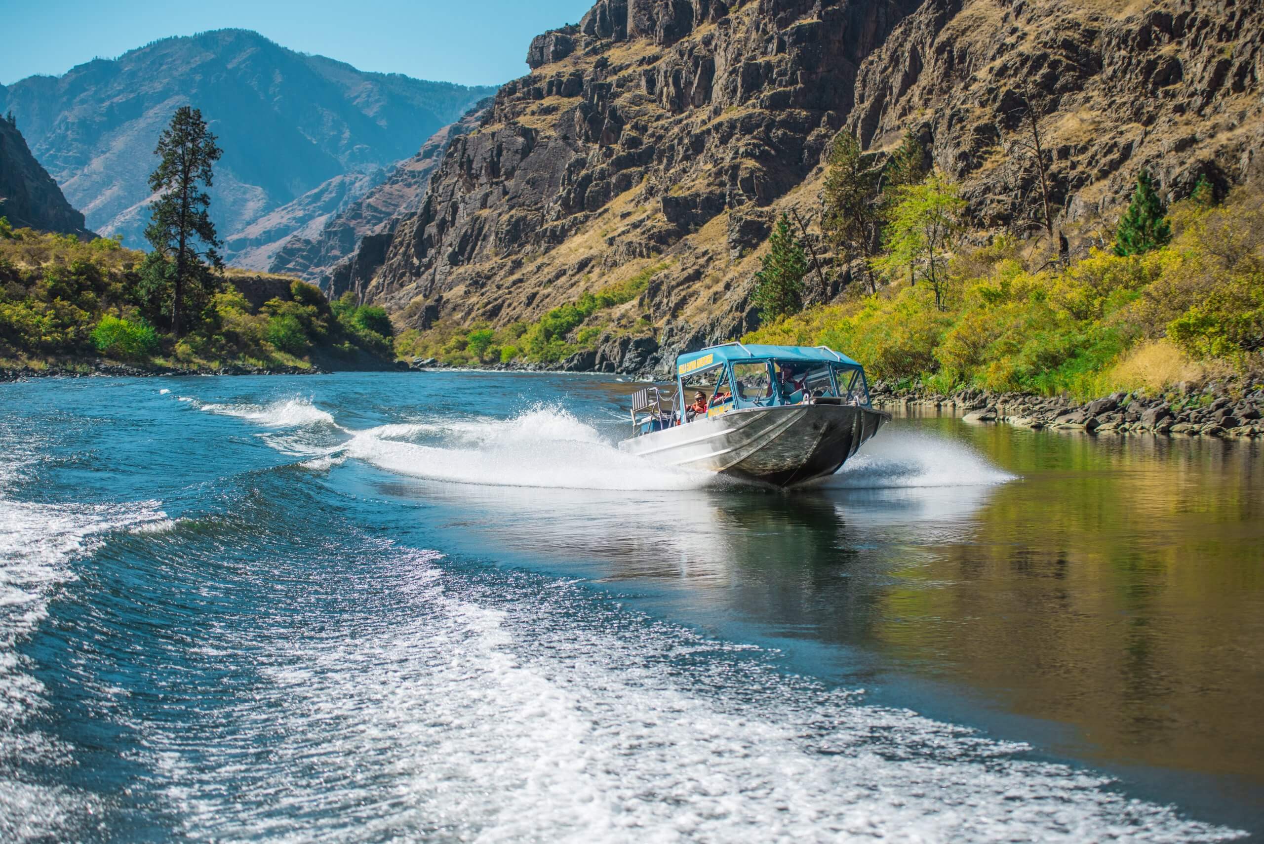 A blue jet boat cruising down a river between two canyon walls.