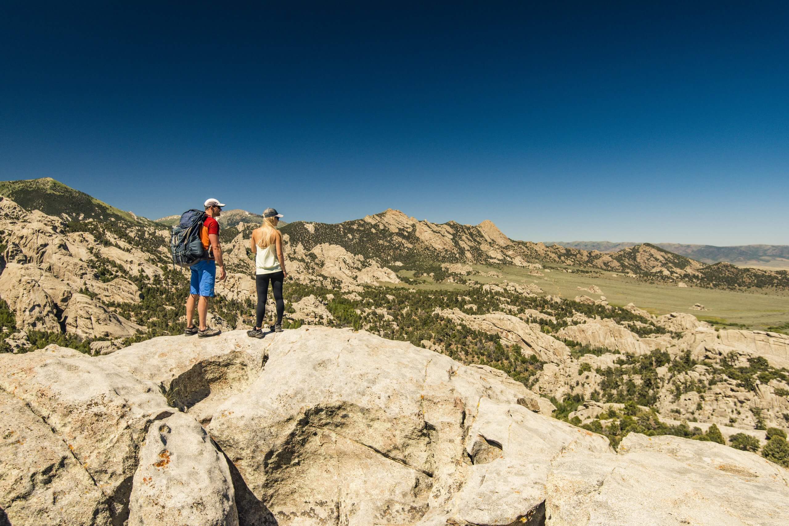 Two people standing on large rocks looking over the City of Rocks National Reserve.