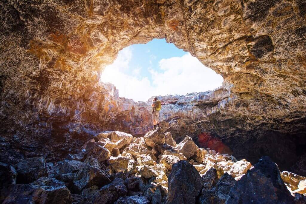 A man standing inside a cave looking up through a natural skylight at Craters of the Moon National Monument and Preserve.
