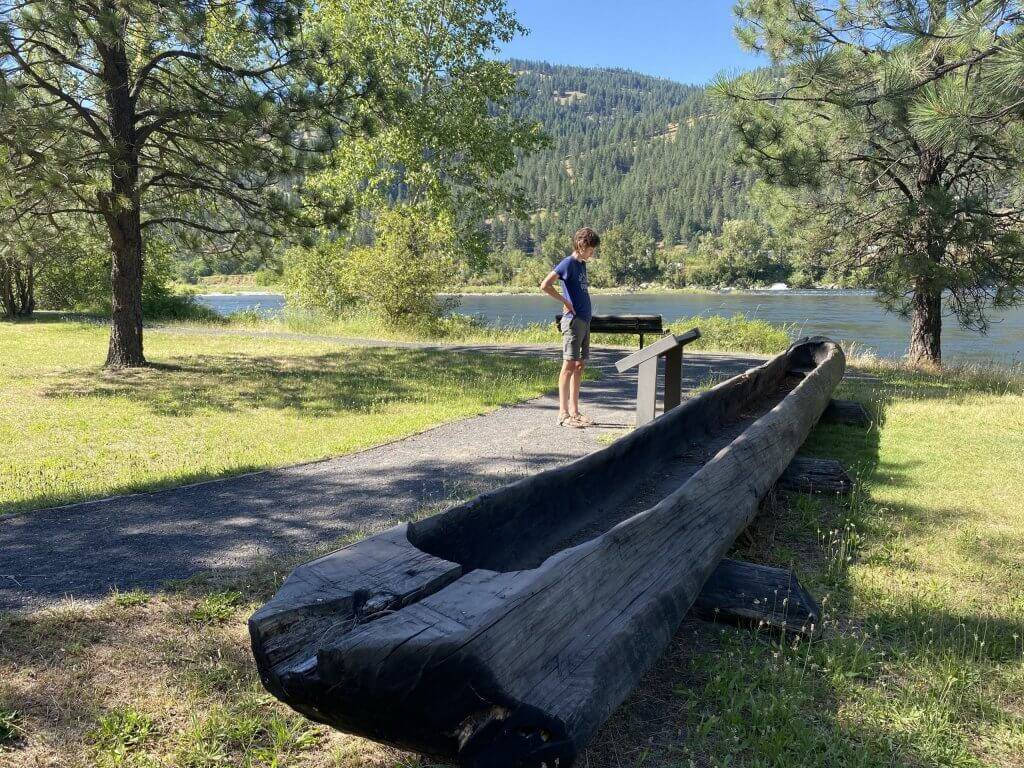 A child standing next to historical canoe reading a informational sign.