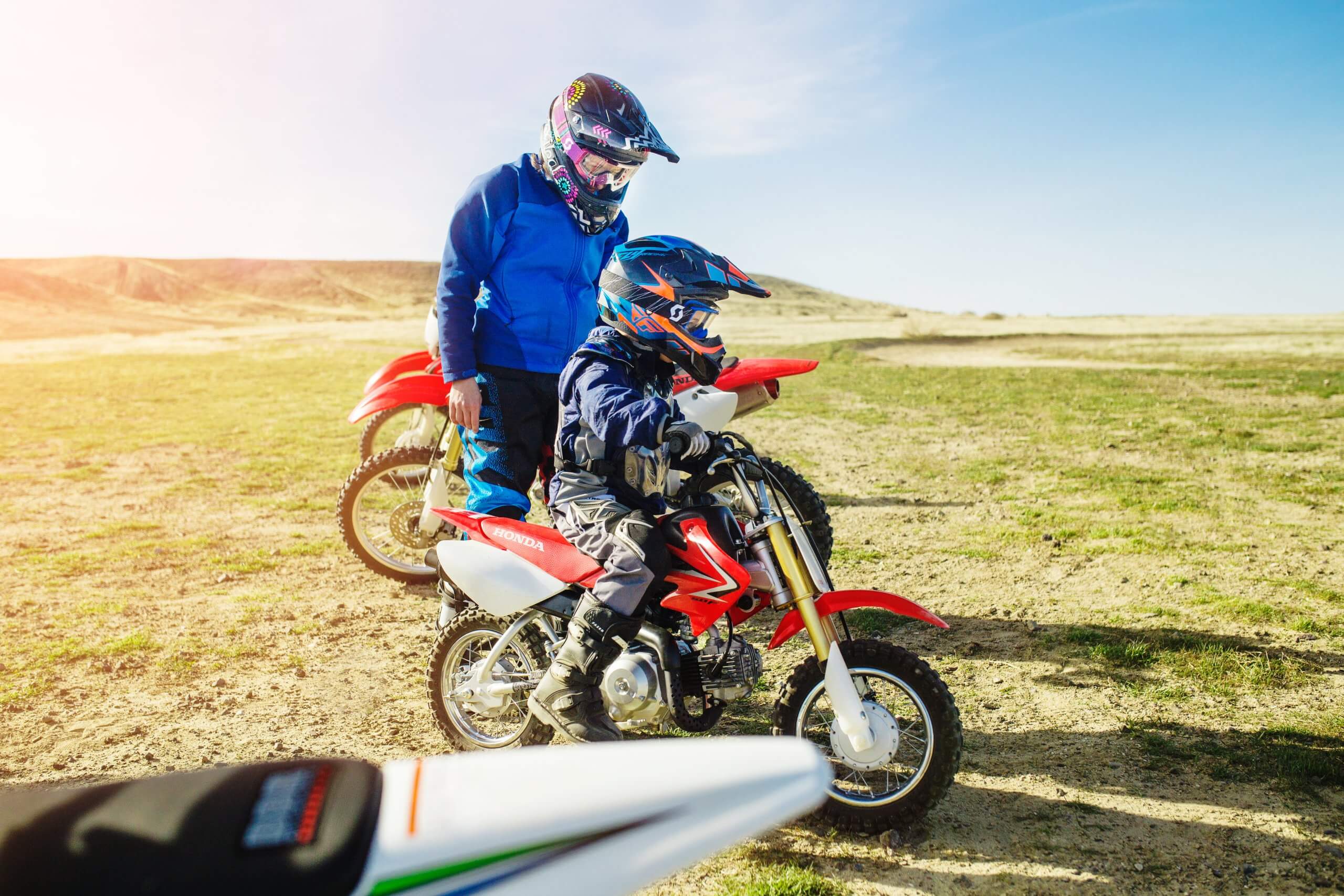 A father and son examining a dirt bike on a trail.