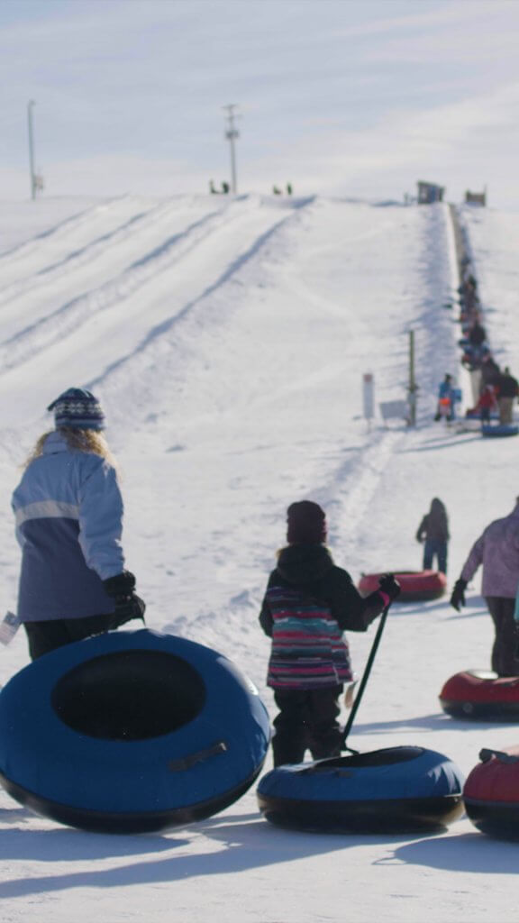 Children and adults walk together up a snowtubing slope at the McCall Activity Barn with tubes in hand during the winter.