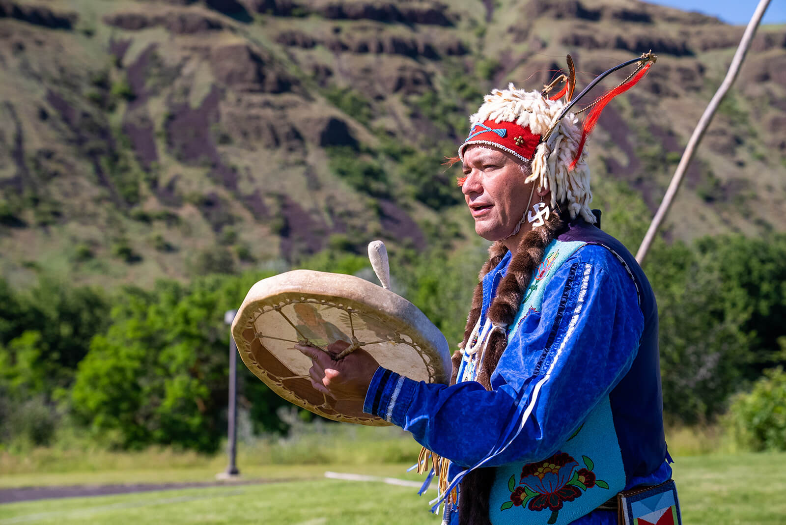 A man wearing traditional Nez Perce clothing playing a drum at Nez Perce National Historical Park.