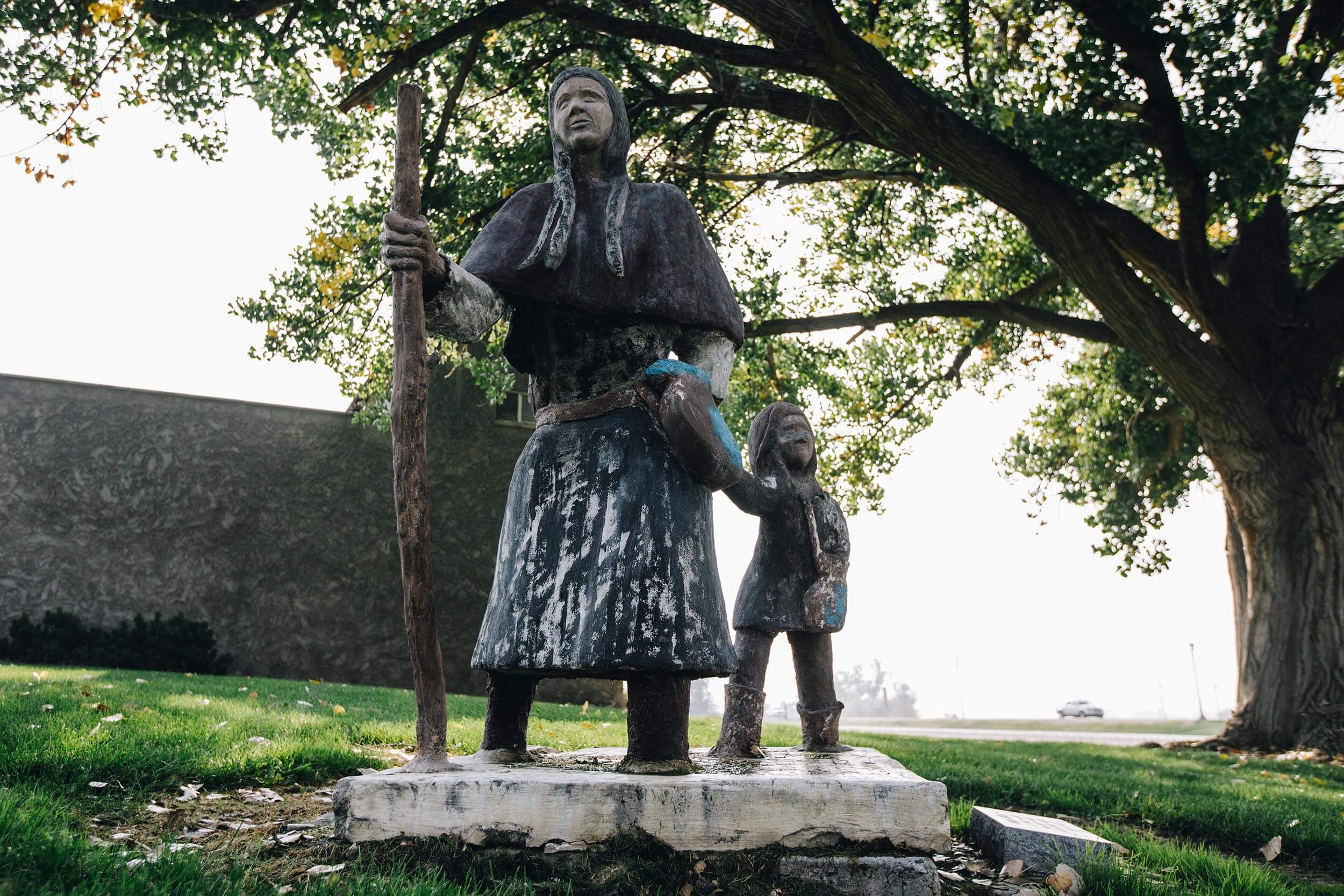 a statue of a woman and child holding hands with a tree in the background