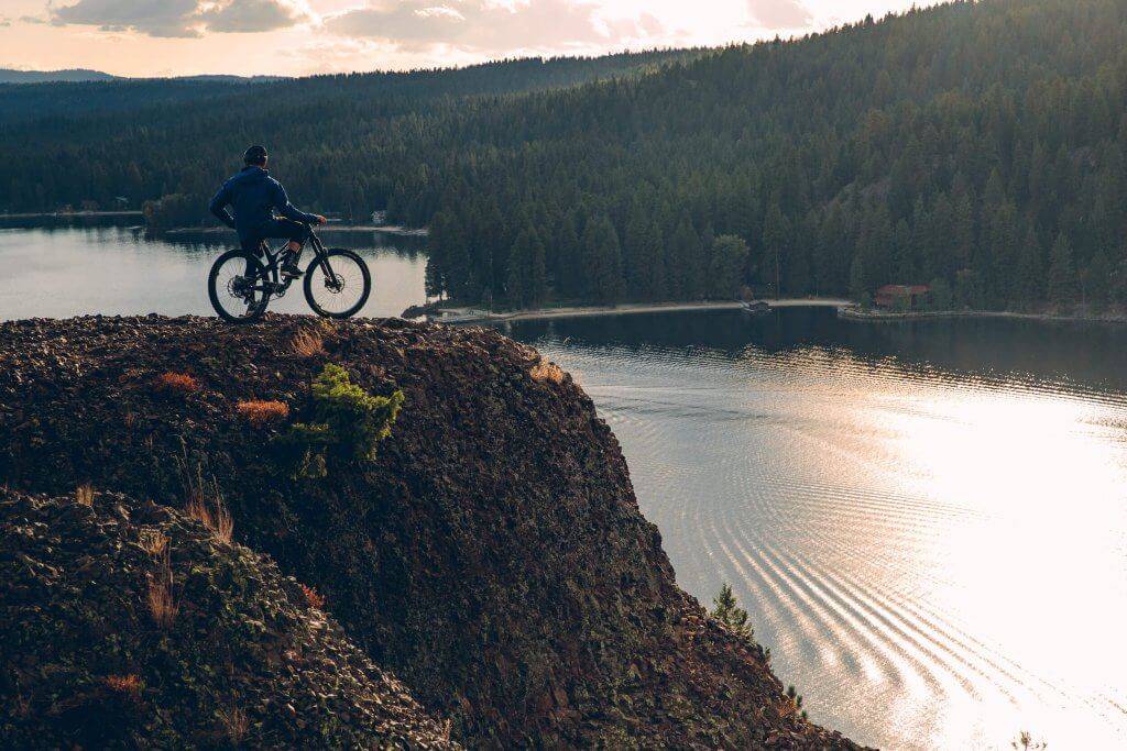 a person on a mountain bike on a hill overlooking a lake with tree covered mountains in the distance