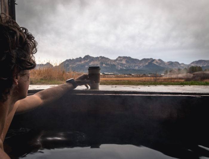 man sipping coffee while soaking in a hot spring