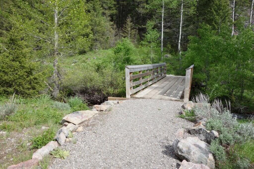 A wide gravel path leads to a wooden planked bridge that crosses over a small creek on the Murdock Creek trail.