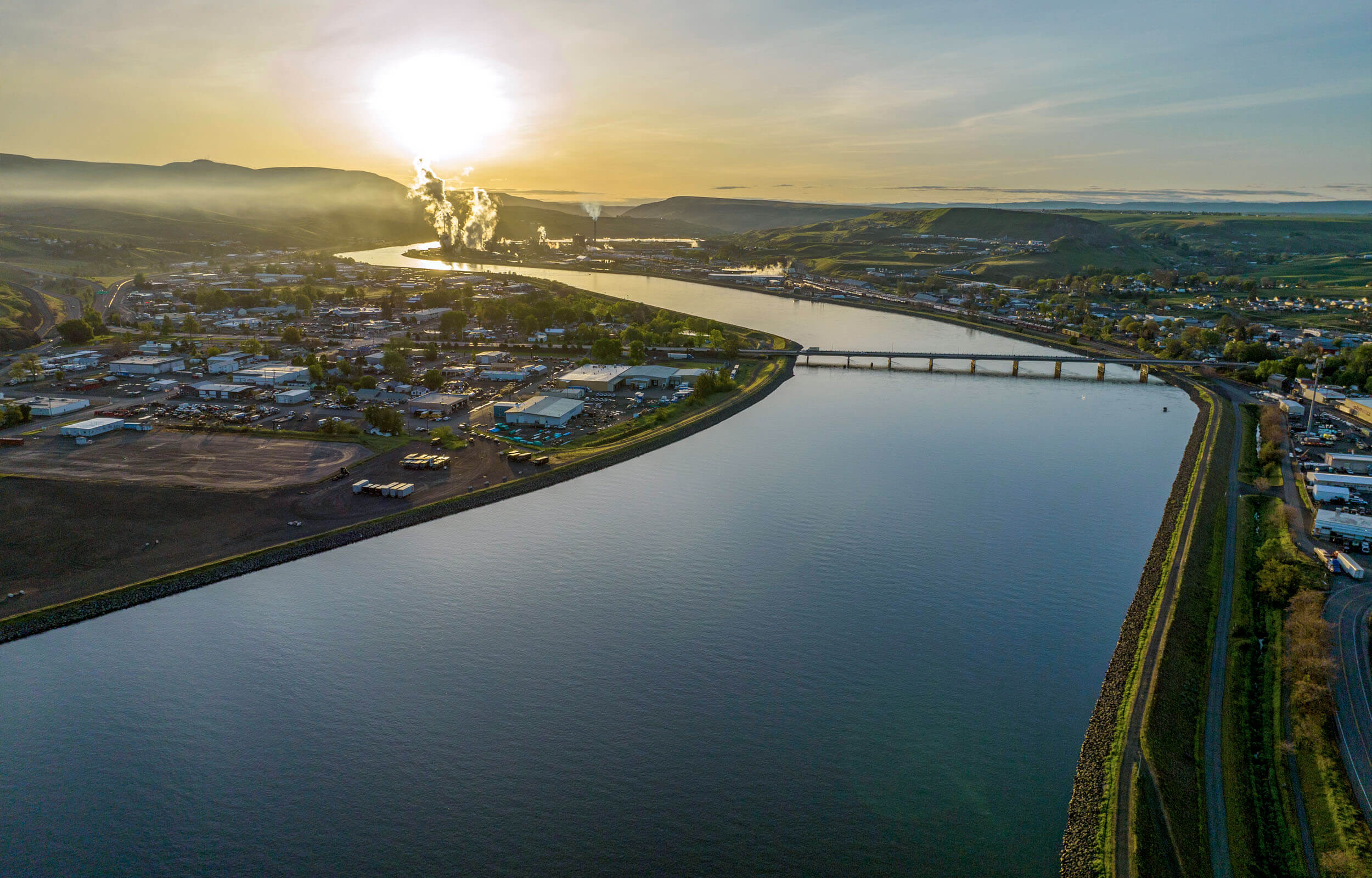 An aerial shot from over the Clearwater River and the town of Lewiston with the sun shining above.
