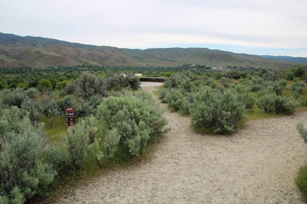 A loose, rocky trail leads to a scenic overlook surrounded by sagebrush.
