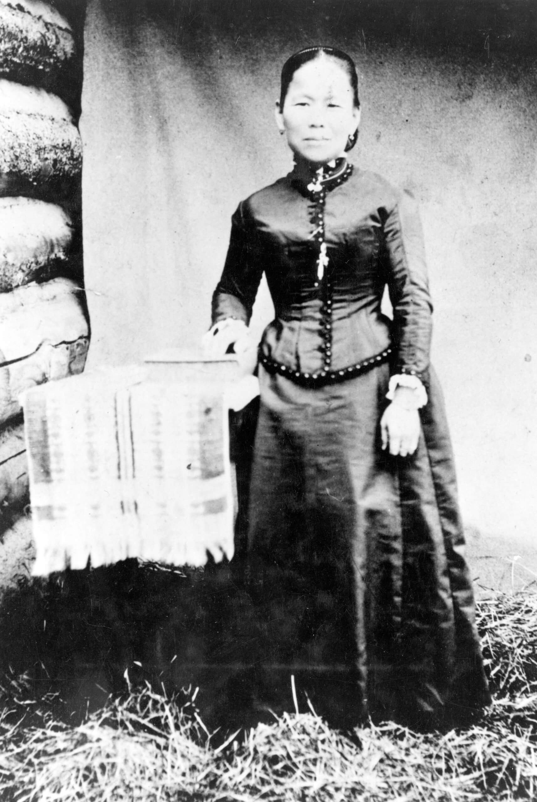 A black-and-white photo of Polly Bemis in her wedding dress, standing next to a table.