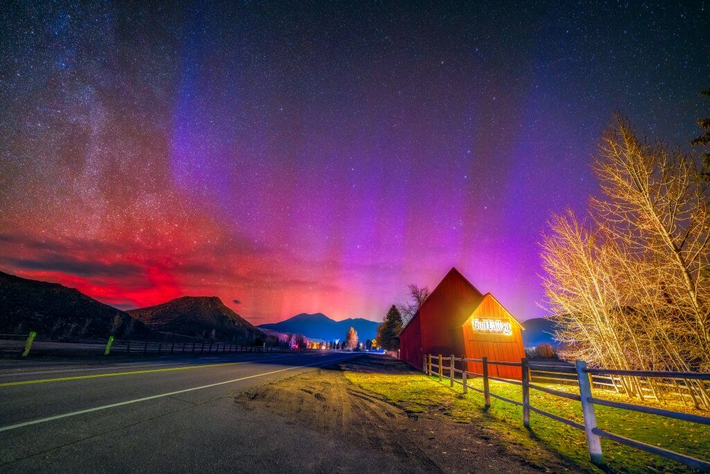 Pink, orange and red northern lights dance in the sky above the Sun Valley barn at night.