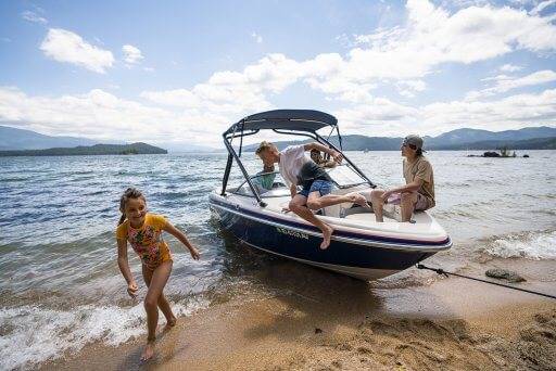 three kids jumping out of a speedboat docked at Priest Lake's beach