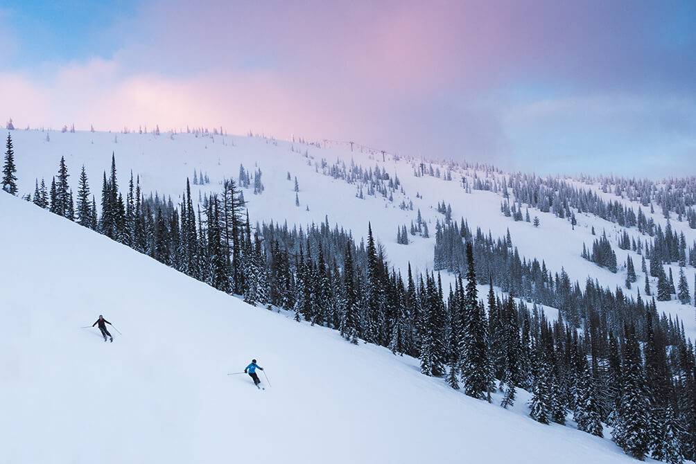 Two people ski down a slope at Schweitzer.