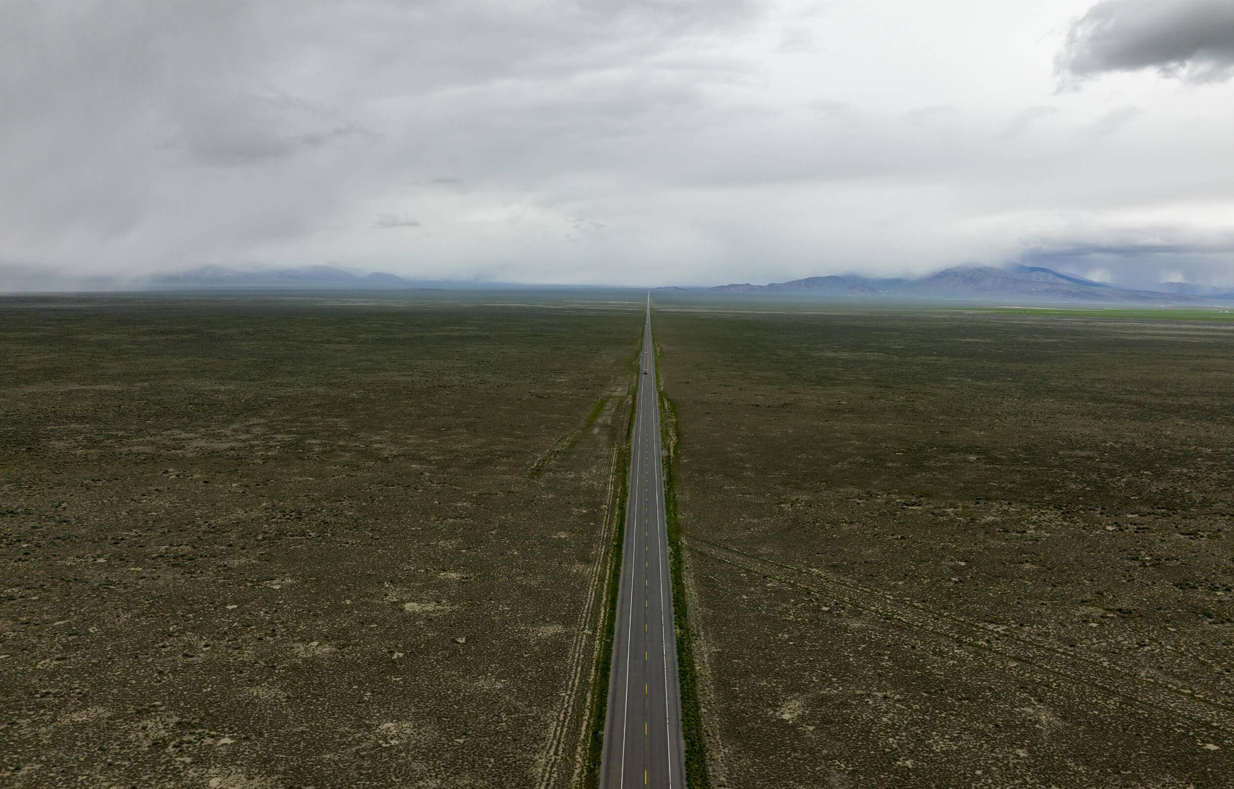 A long stretch of road surrounded by wide open fields, with mountains in the distance.