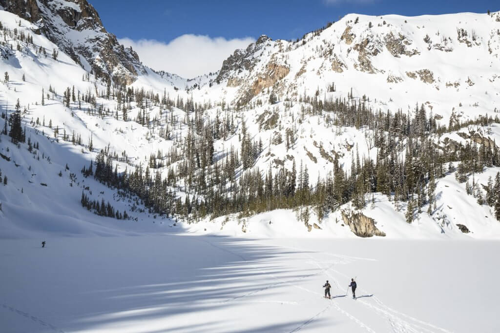 Two people in ski and snow gear backcountry ski in the Sawtooth Mountains, near Stanley.