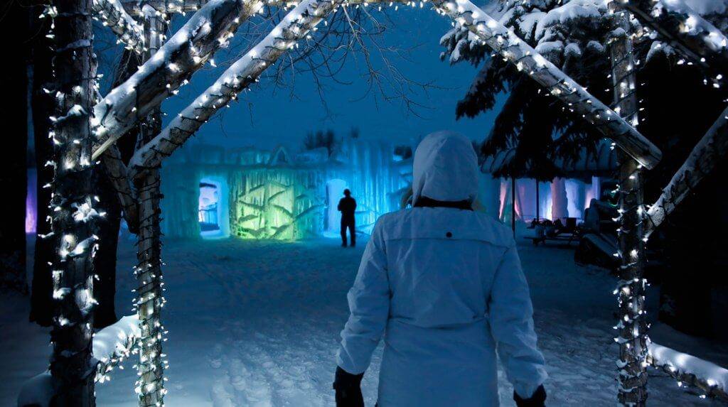 woman in snow clothing walking towards illuminated ice castle