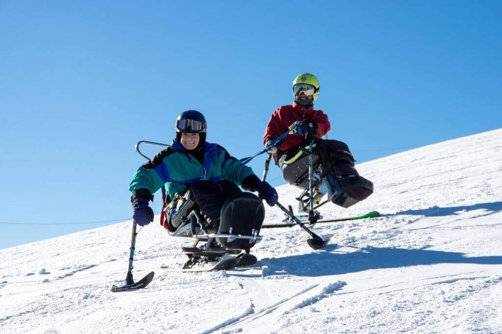 a ski instructor in a sit ski working with a sit ski student on snowy slope