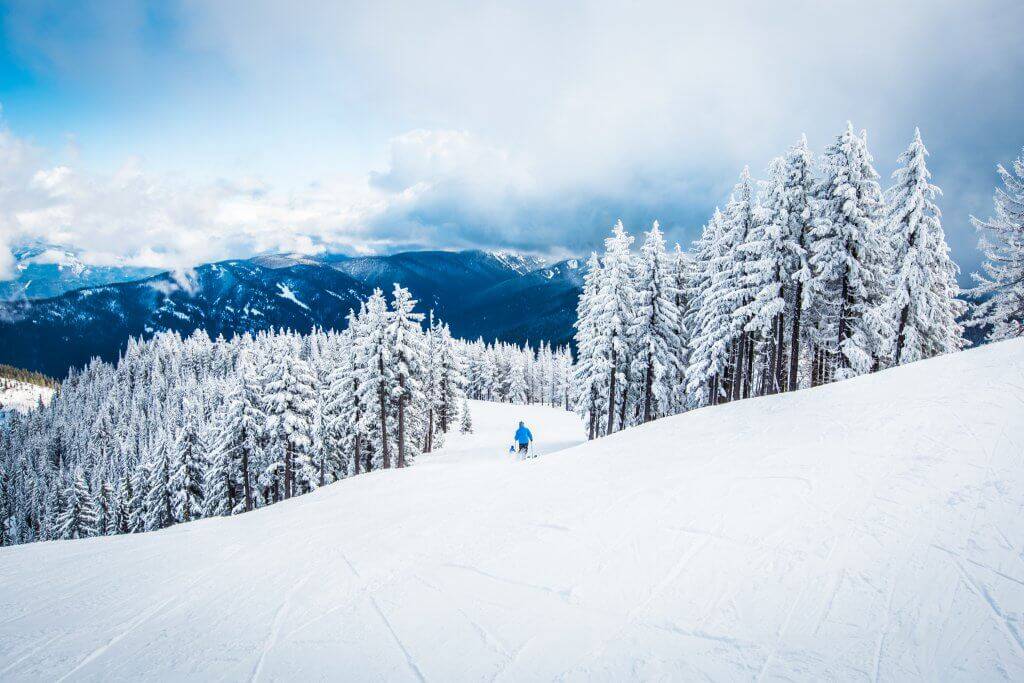 A person in outdoor gear skiing at Silver Mountain Resort surrounded by snowy peaks in the winter.