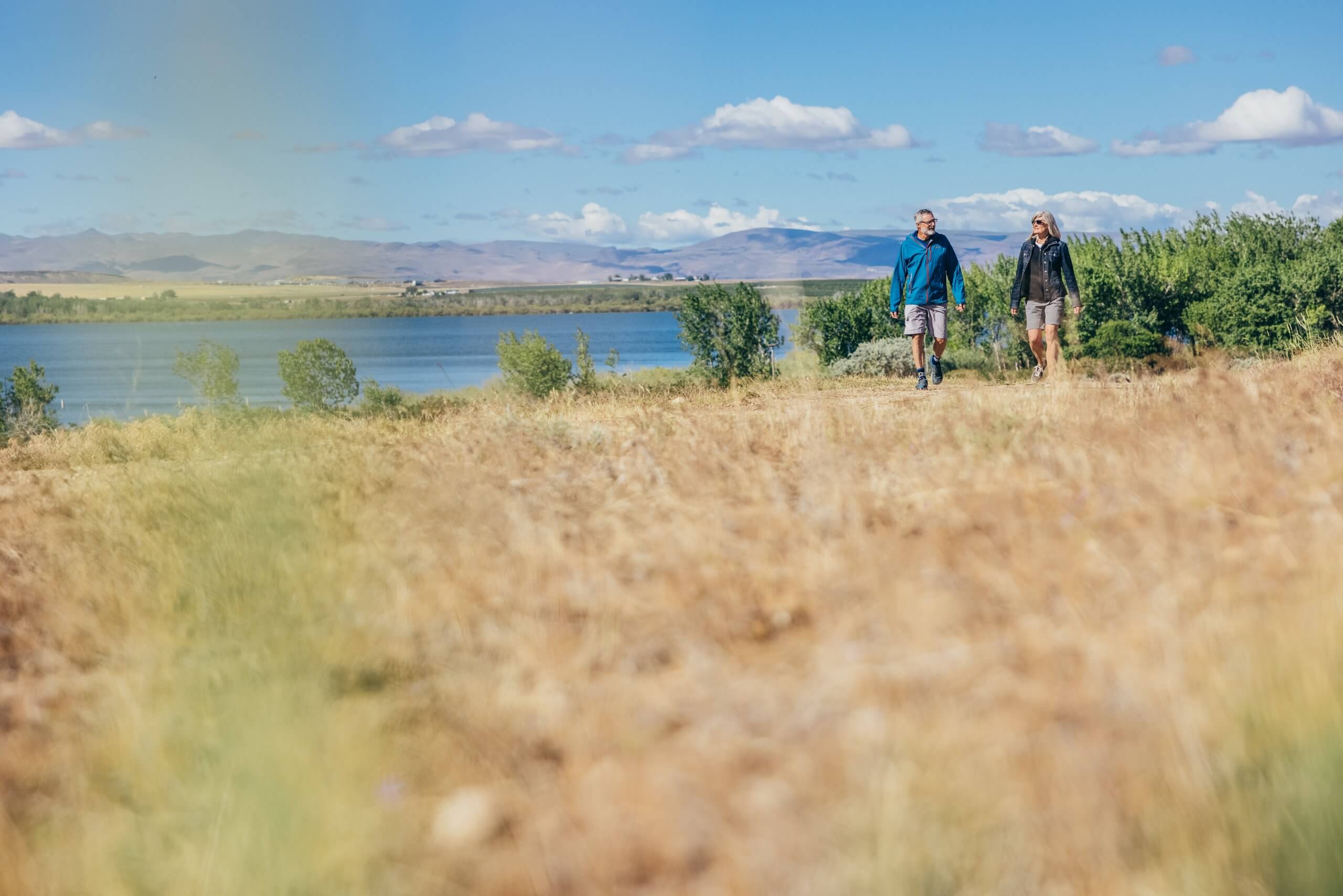 two people walking at a wildlife refuge beside a lake with mountains in the distance