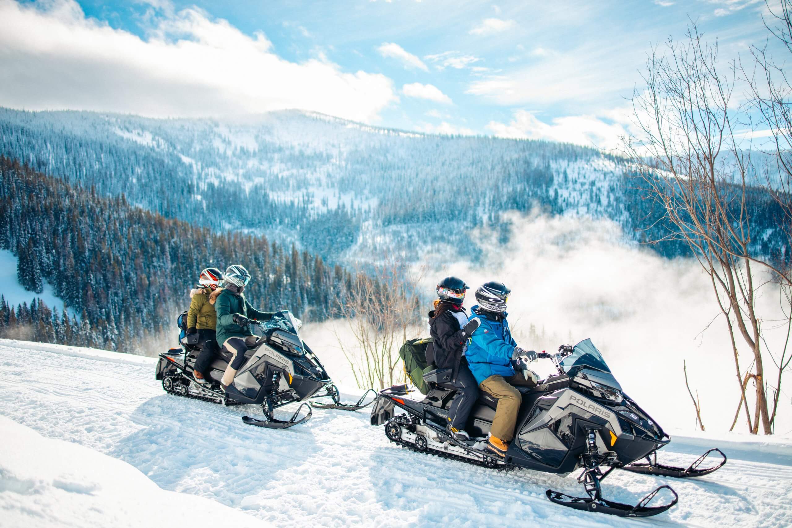 Two couples look out over the landscape while snowmobiling on a mountain trail near Sandpoint.
