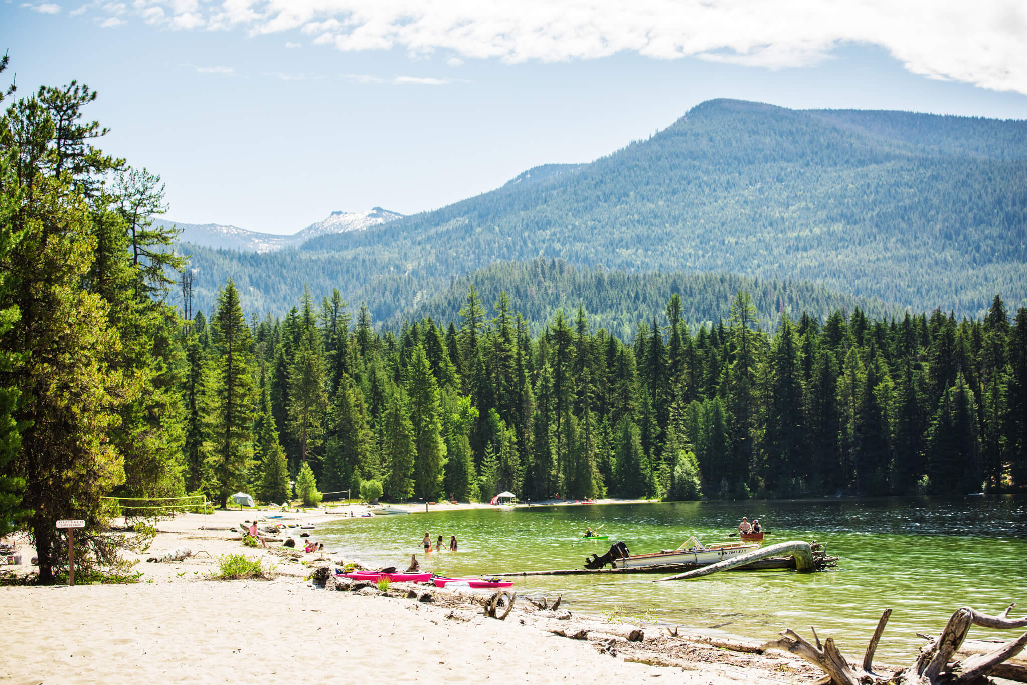 Several people relaxing on the beach and playing in the water at Priest Lake in Priest Lake State Park.
