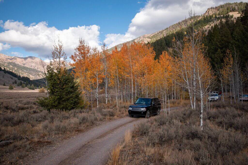 a black SUV driving on a dirt road with orange and red aspen trees in the background