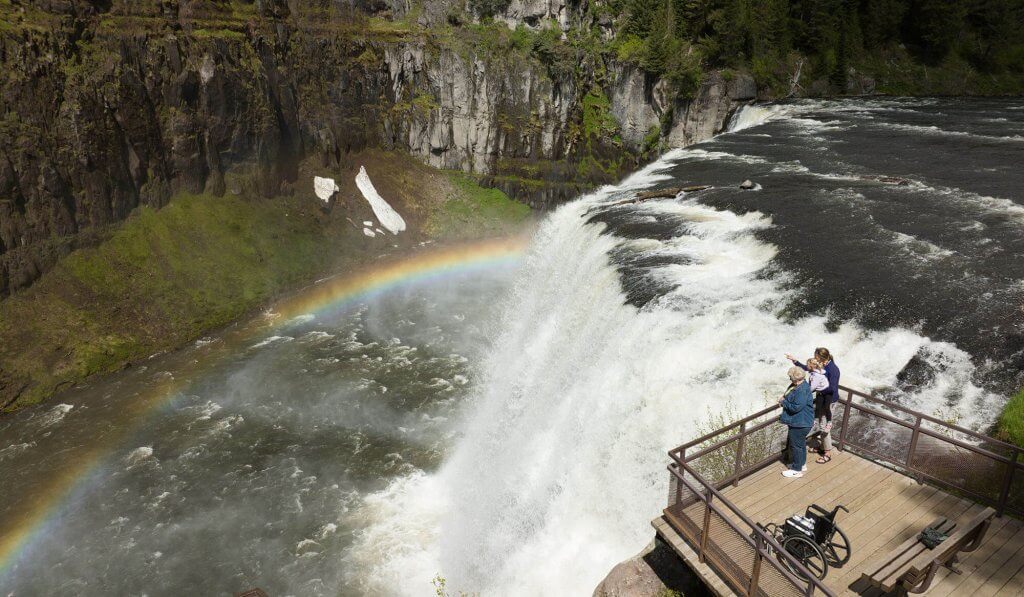 Three people stand on an observation deck overlooking Upper Mesa Falls.
