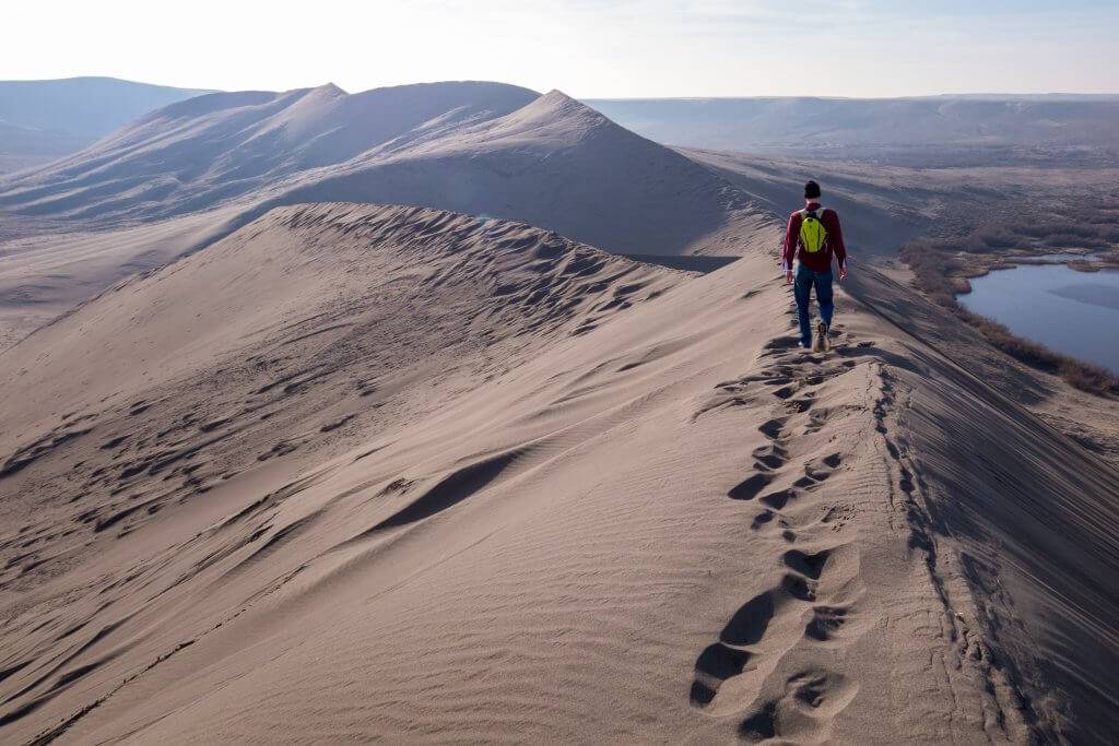 man walking on ridge of sand dune