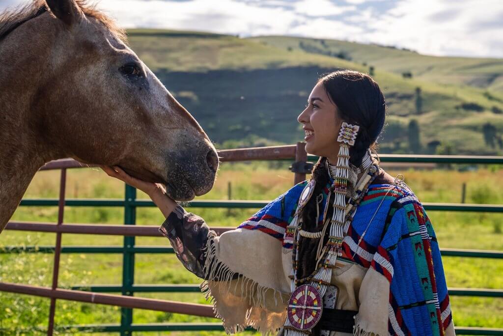 A woman wearing traditional Nez Perce clothing standing next a horse at Nez Perce National Historical Park.