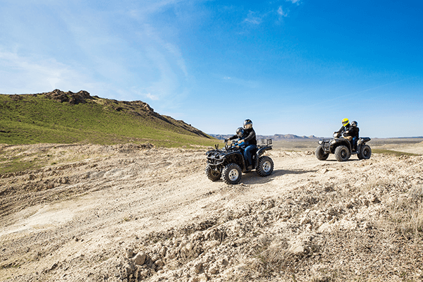 People riding two ATVs with mountains in the background.